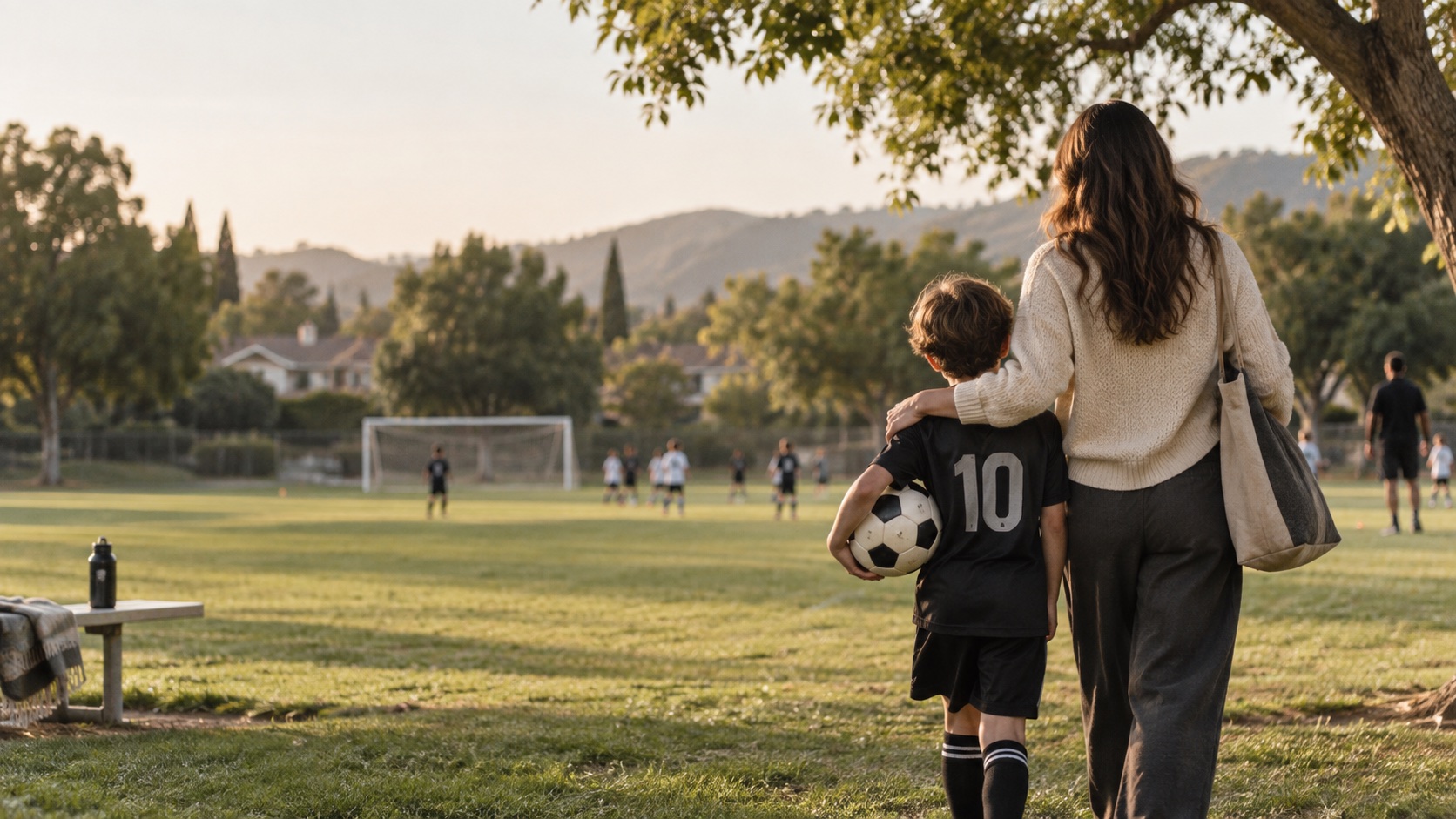A parent walking a young soccer player across the field at golden hour